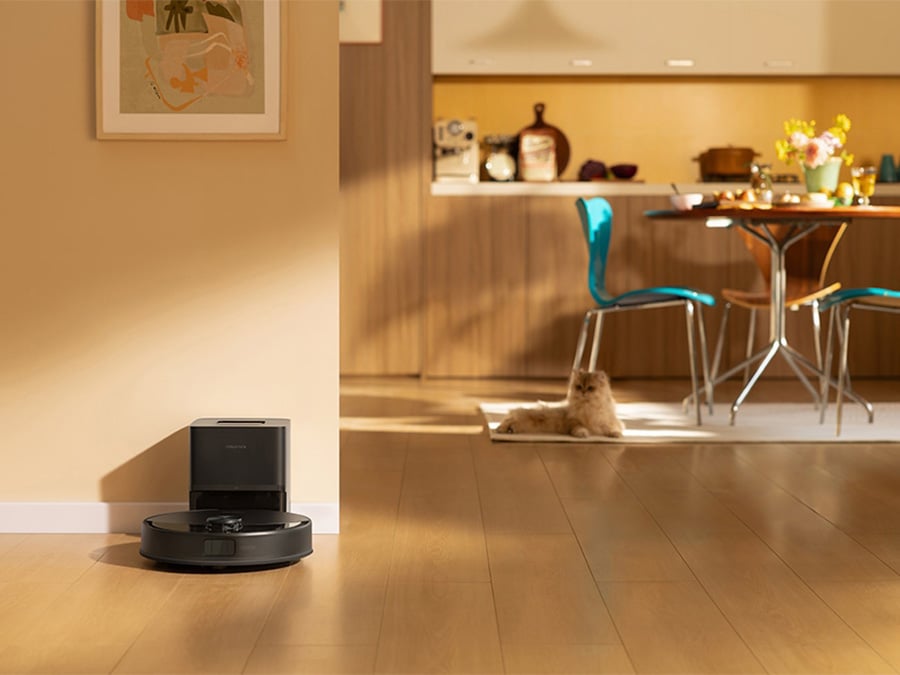 Robot Roborock Q10 VF ładujący się w stacji dokującej, w tle widoczna kuchnia z kotem leżącym na dywaniku
