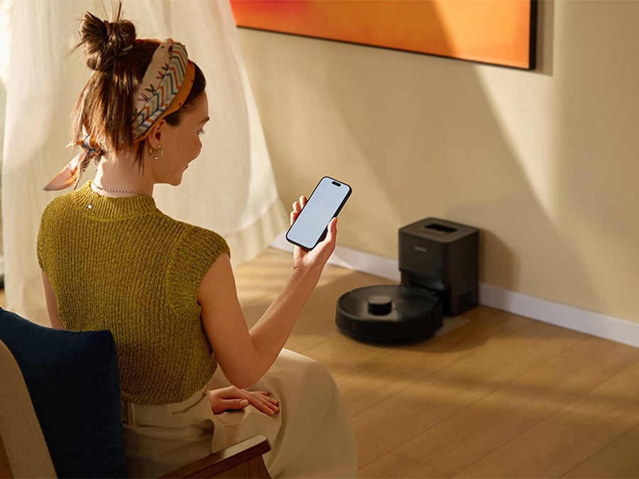 Kobieta siedząca w jasnym salonie steruje robotem sprzątającym Roborock Q7 TF Black za pomocą aplikacji mobilnej