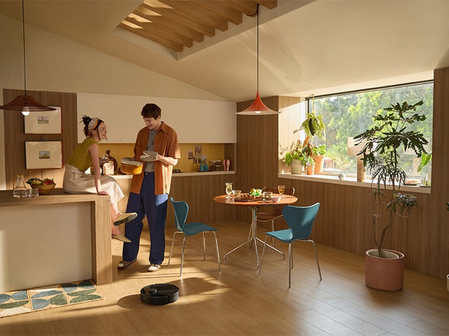 Robot Roborock Q10 PF Black sprząta w kuchni, w tle para przygotowująca posiłek