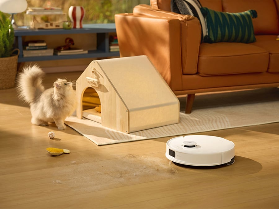 Robot sprzątający Roborock Q10 PF White odkurza podłogę w salonie, obok niego biały kot i domek dla zwierzaka