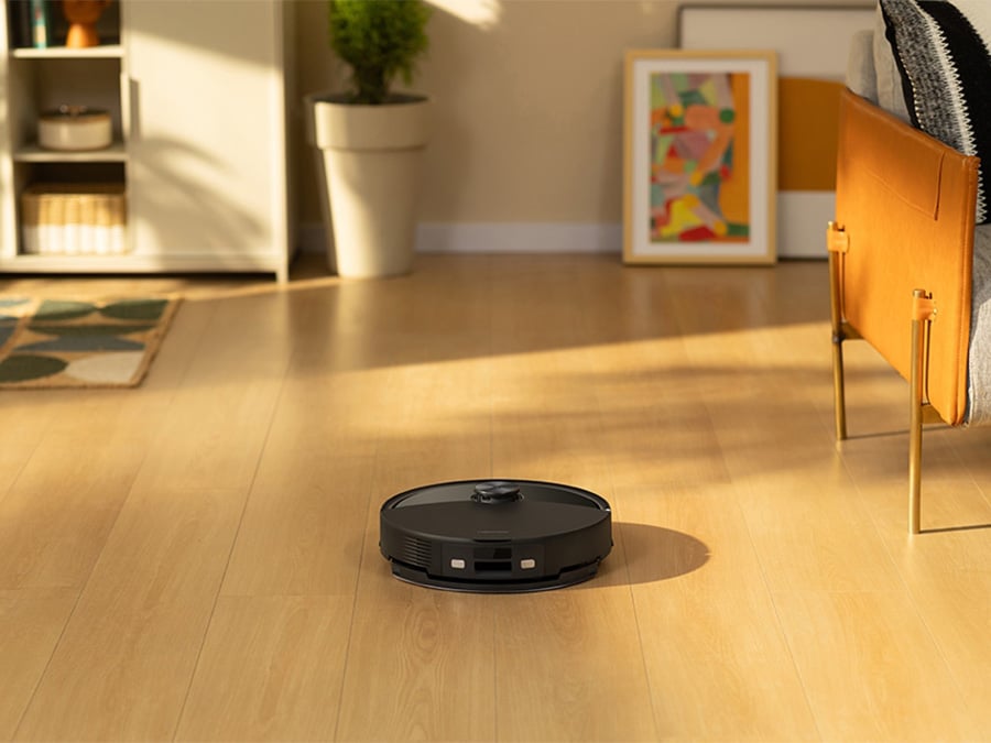 Kobieta siedząca w salonie i obsługująca robota sprzątającego Roborock Q10 VF za pomocą aplikacji na smartfonie