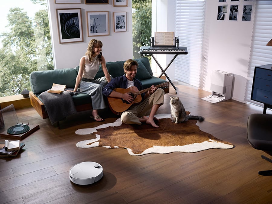 Kobieta i mężczyzna spędzają czas w salonie z kotem, podczas gdy robot sprzątający Roborock Qrevo Edge T White cicho odkurza podłogę drewnianą