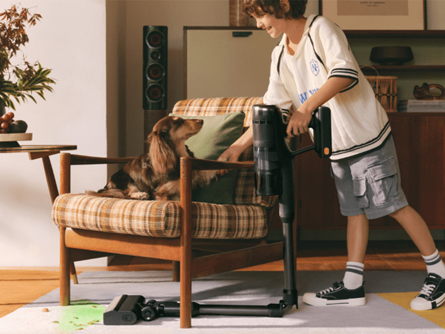 Chłopiec z odkurzaczem Roborock H60 Ultra Black przy fotelu, w którym siedzi pies — sprzęt gotowy do sprzątania sierści