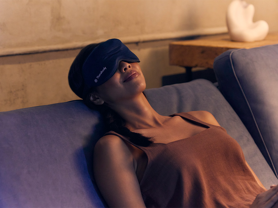 Kobieta odpoczywa na kanapie w masce Therabody sleep mask, widok z boku