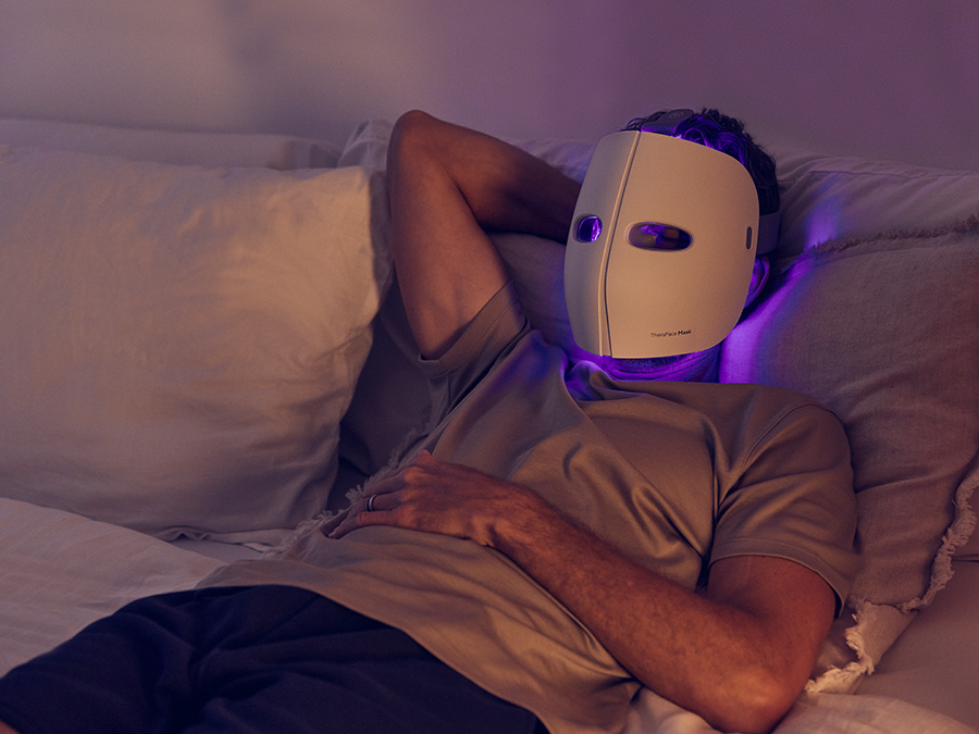 Mężczyzna leżący w łóżku i korzystający z Therabody TheraFace Mask