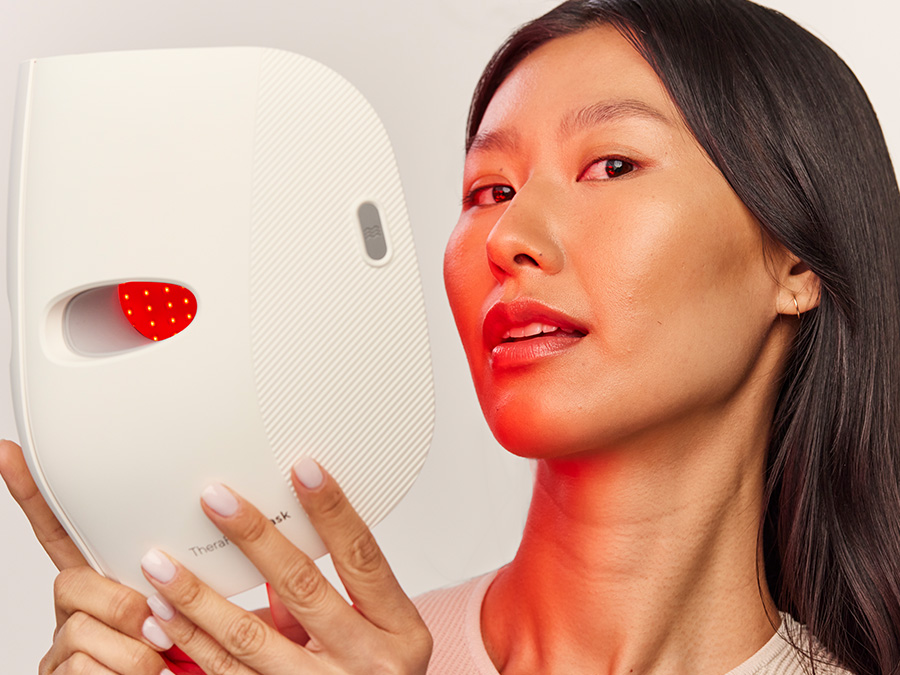 Zbliżenie na kobietę trzymającą Therabody TheraFace Mask z włączoną czerwoną diodą LED