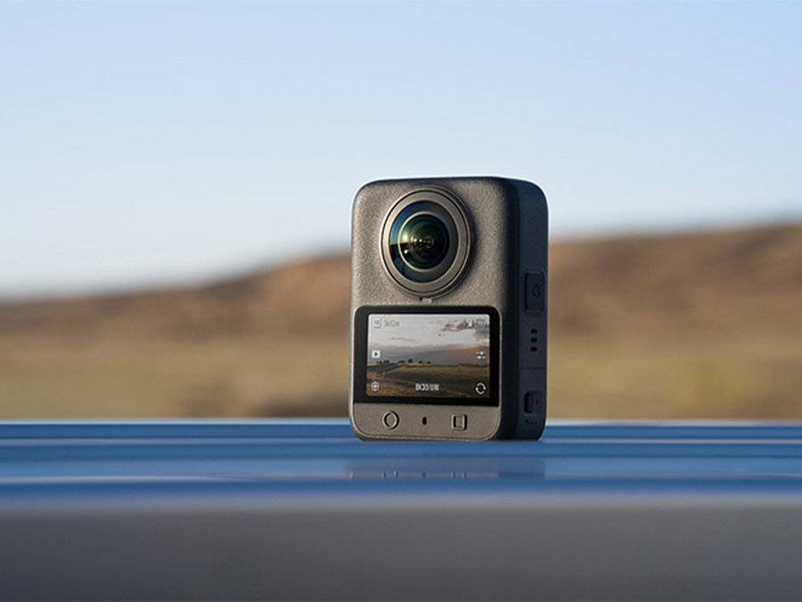 Kamera DJI Osmo 360 stojąca na metalowej powierzchni na tle krajobrazu z zamontowaną osłoną obiektywu