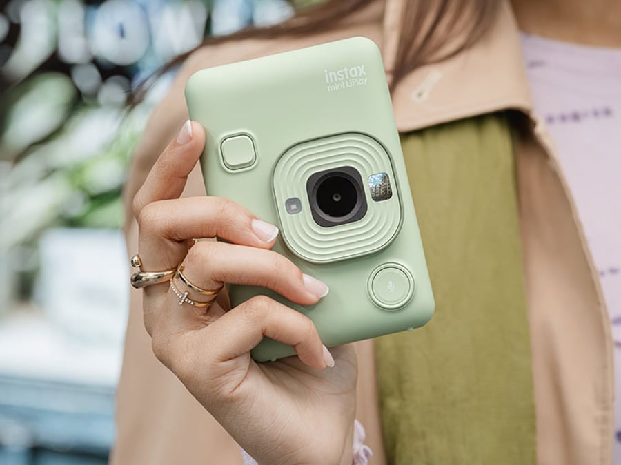 Zielony aparat Fujifilm Instax mini LiPlay trzymany w dłoni w kobiecej stylizacji
