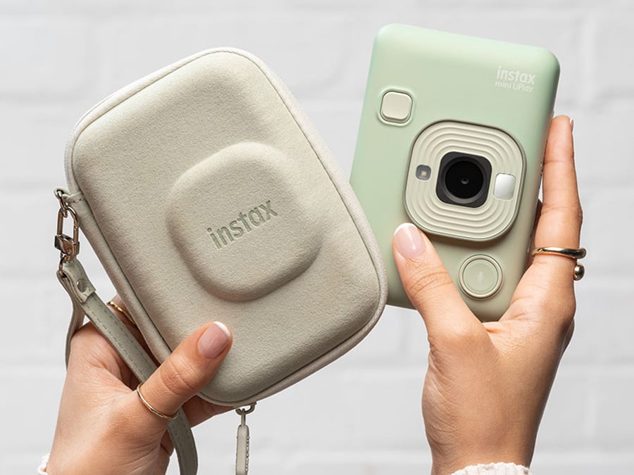 Zielony aparat Fujifilm Instax mini LiPlay obok etui, trzymany w obu dłoniach