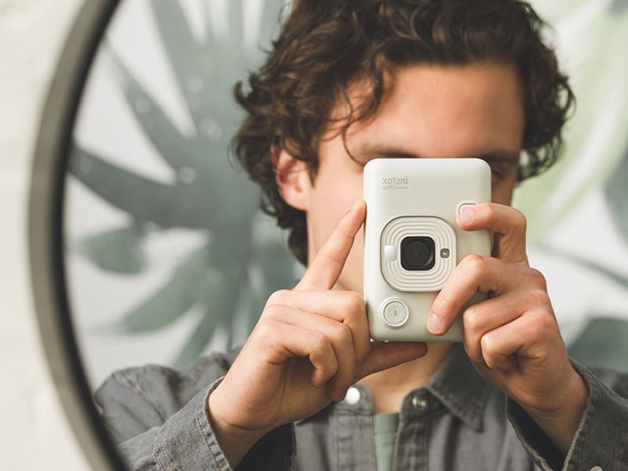 Mężczyzna trzymający biały aparat Fujifilm Instax mini LiPlay w dłoniach