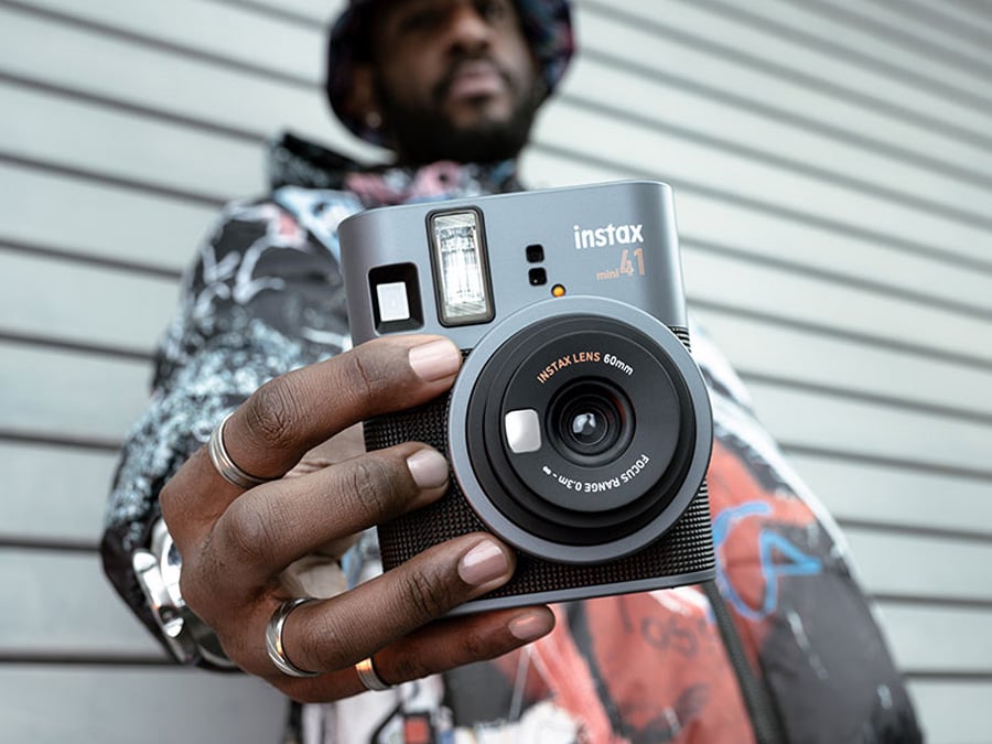 Zbliżenie na ręce trzymające Fujifilm Instax mini 41 z widocznym pierścieniem regulacji trybu