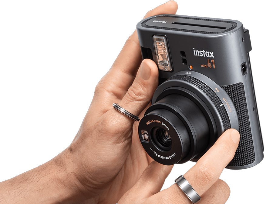 Mężczyzna prezentuje aparat Fujifilm Instax mini 41 trzymany w dłoni z widoczną soczewką