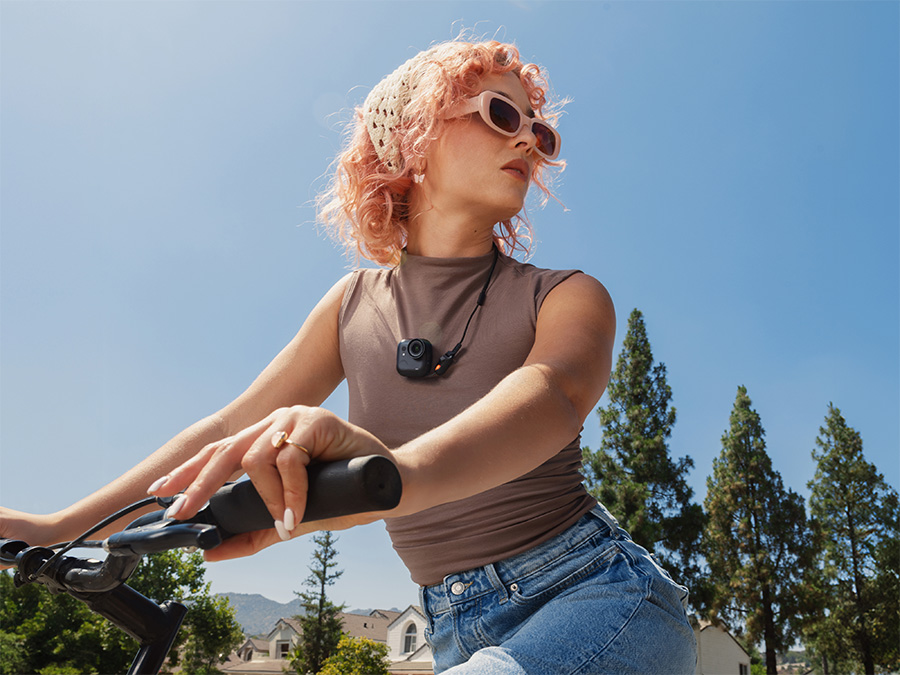 Kobieta jadąca na rowerze z kamerą Insta360 GO Ultra zawieszoną na smyczy na piersi; rejestracja ujęć podczas ruchu