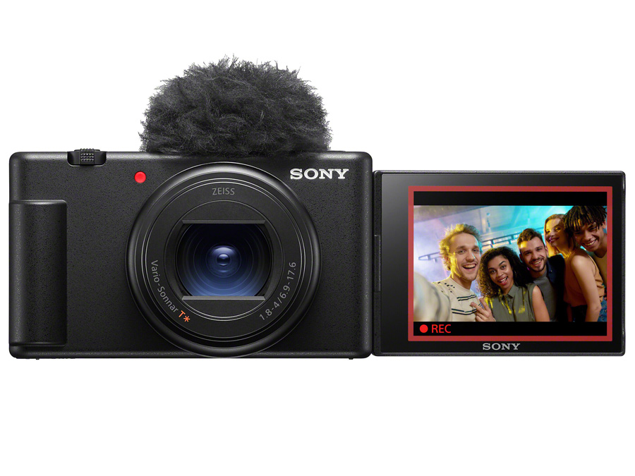 Aparat Sony ZV-1 II z podłączonym mikrofonem i rozkładanym ekranem prezentującym nagranie grupy osób