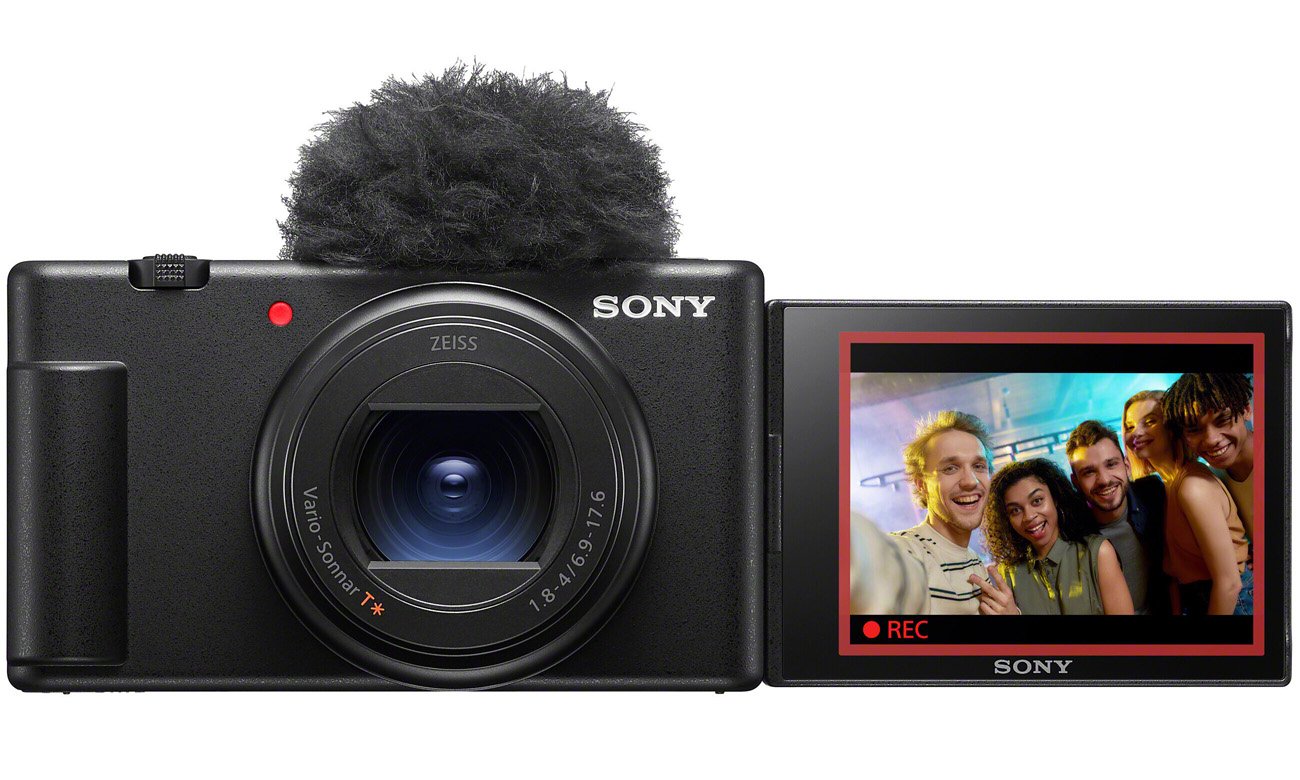 Aparat Sony ZV-1 II z podłączonym mikrofonem i rozkładanym ekranem prezentującym nagranie grupy osób
