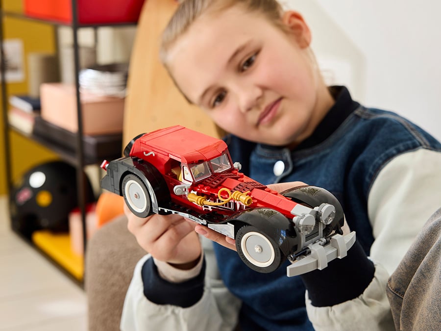 Dziewczynka trzyma w dłoniach zbudowany czerwono-czarny samochód LEGO inspirowany Cruellą de Mon i przygląda się mu z bliska